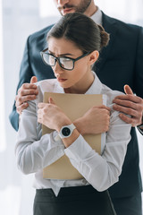 cropped view of businessman hugging scared secretary in office