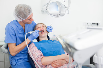 Professional dentist examining and performing treatment to young woman