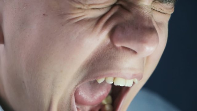 Angry young man screaming opening his mouth, close-up