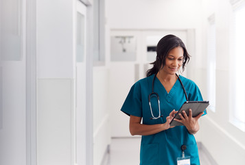 Female Doctor Wearing Scrubs In Hospital Corridor Using Digital Tablet - Powered by Adobe