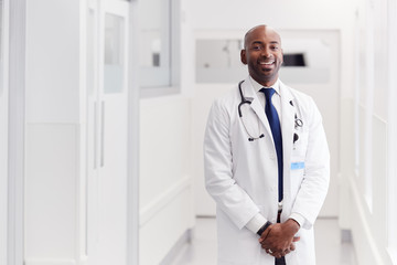 Portrait Of Mature Male Doctor Wearing White Coat Standing In Hospital Corridor