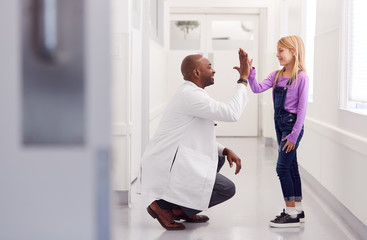 Male Paediatric Doctor Giving Young Girl Patient High Five In Hospital Corridor - Powered by Adobe