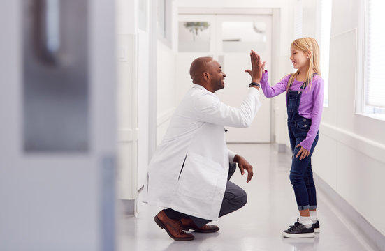 Male Paediatric Doctor Giving Young Girl Patient High Five In Hospital Corridor