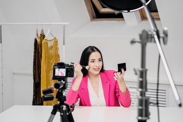 A beautiful young woman blogger in a pink jacket shoots a blog about cosmetics.