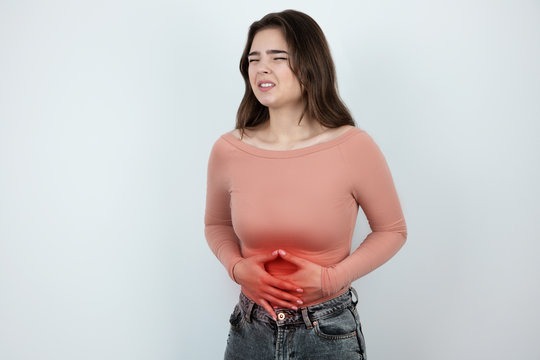 young beautiful woman suffering from pain in her stomach looking helpless on isolated white background, healthcare concept