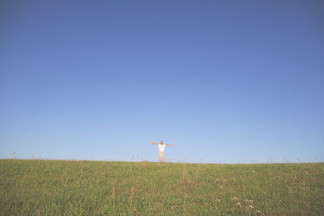 boy spreading his arms on a green meadow against blue cloudless sky.