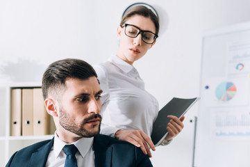 Obraz premium attractive secretary with folder touching shoulder of businessman in office