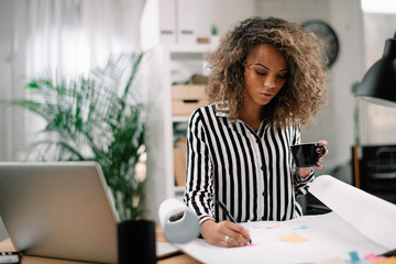 Beautiful african businesswoman in office. Woman at work drinking coffee while working. 