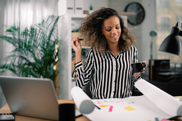 Beautiful african businesswoman in office. Woman at work drinking coffee while working. 