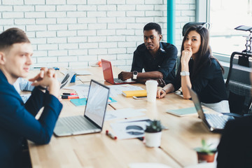 Pensive adult multiethnic employees working on complex project together in loft office