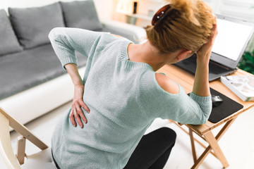 Woman working on a laptop and having headache and back, hip, spine pain.