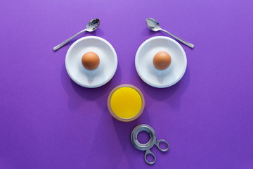 Fun breakfast concept with abstract astonished human face made of breakfast items on purple background.