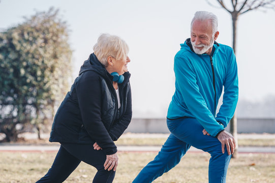 A senior adult male teaching a senior woman how to stretch in the park.
