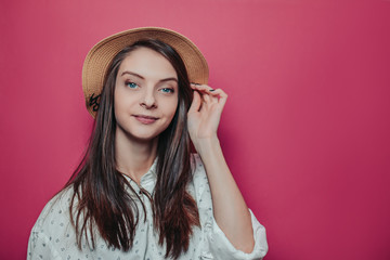 Pretty long haired woman in a straw hat on pink background.