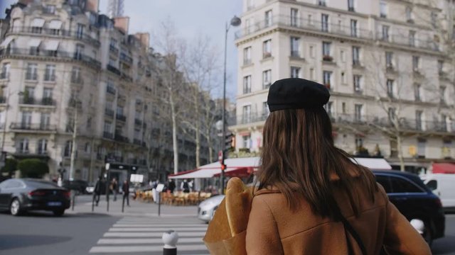 Cinematic move on beautiful happy tourist woman walking along busy Paris street with paper shopping bag slow motion.