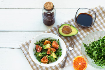 Salad of avocado, orange and arugula with soy sauce and sesame seeds on a white wooden table. Top view.
