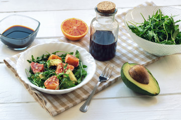 Salad of avocado, orange and arugula with soy sauce and sesame seeds on a white wooden table.