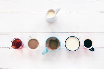 Five different hot drinks on white wooden table. Hot chocolate with cinnamon, matcha tea, coffee...