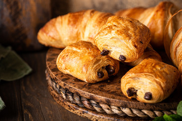 Coffee break with freshly baked sweet buns puff pastry with chocolate and croissants on old wooden background. Breakfast or brunch concept
