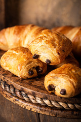 Coffee break with freshly baked sweet buns puff pastry with chocolate and croissants on old wooden background. Breakfast or brunch concept