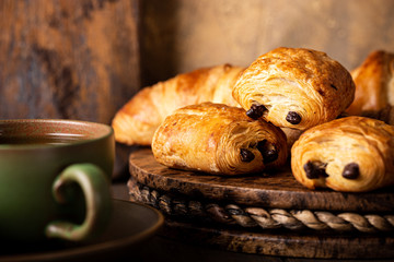 Freshly baked sweet buns puff pastry with chocolate and croissants on old wooden background. Breakfast or brunch concept