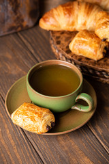 Green cup of tea with mini chocolate bun, puff pastry on old wooden table. Tasty tea break concept, copy space.