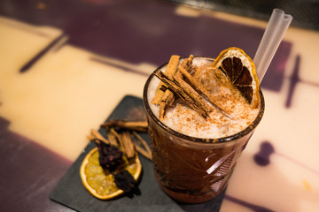 orange cocktail with dried orange slice and plastic straws and cinnamon sticks indoor on bar top at...