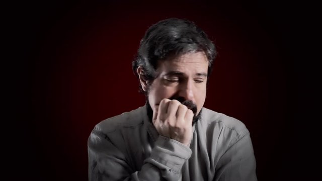 An awkward man's expression. Medium close-up shot of the face over a red background. Part of a series of depictions of feelings and emotions with professional actors.
