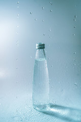 Glass bottle and water splashes and falls on white blue background. Freshness and life-giving power of water. Thirst