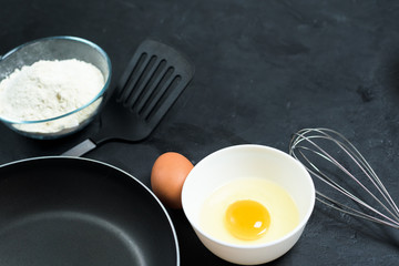 Maslenitsa.Ingredients for baking pancakes. frying pan, eggs, flour, egg beater, on a black background top view. top view, place to copy text, recipe.