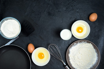 Maslenitsa.Ingredients for baking pancakes. frying pan, milk, eggs, flour, egg beater, on a black background top view. baking background, top view, place to copy text, recipe.