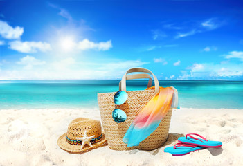 Fototapeta na wymiar Concept summer holiday. Accessories - bag, straw hat, sunglasses with palm tree reflection, pareo, flip-flops on sandy beach against ocean, blue sky, clouds and bright sun. Beautiful colorful image.