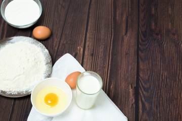 Maslenitsa is a traditional holiday in February . Ingredients for baking pancakes. eggs, flour, egg beater, on a dark wooden background top view. top view, place to copy text, recipe.