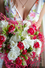 A young woman is holding a colorful blossoming flower bouquet of red and white roses and freesia. Romantic gift for the girl. Background blur.