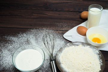 Maslenitsa is a traditional holiday in February . Ingredients for baking pancakes. eggs, flour, egg beater, on a dark wooden background top view. top view, place to copy text, recipe.