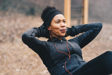 A young woman doing situps outdoors while listening to the music.