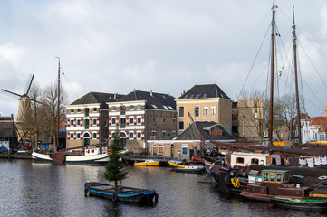 Museum harbor in Gouda, with flour mill De Roode Leeuw, monumental inland vessels, and a boat with a Christmas tree in the foreground.