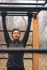 A woman using outdoor exercise equipment - horizontal ladder.