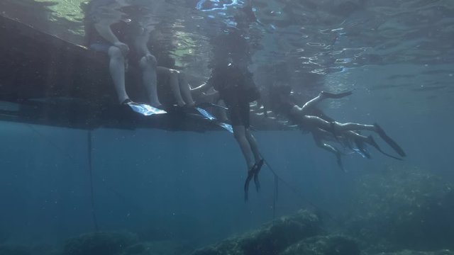 Group of snorkelers and scuba divers are sitting on a floating platform. Underwater view.