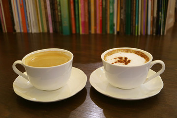 Black Coffee and Cappuccino Coffee with Blurry Rows of Books in Background