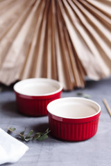 Small glazed ceramic ramekin. Red baking cup for cupcakes, muffins on a gray and white background. Ceramic baking dish.