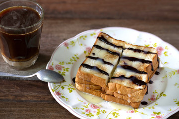 Toasted toast pour with sweetened condensed milk and chocolate in white dish flower patterned and black coffee in glass