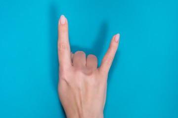 Adult white woman showing rock and roll hand sign isolated on bright blue background. Horizontal top view photography of beautiful female hand with mat pastel natural pink manicure.