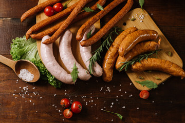 Different smoked sausages with vgetables and ingredients on wooden background