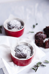 Chocolate muffins in red cups. Small glazed ceramic ramekin with brown cakes on a gray and white background.