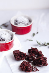 Chocolate muffins in red cups. Small glazed ceramic ramekin with brown cakes on a gray and white background.