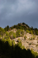 The high-contrast view of the low French Alps under the warm sunlight against the background of the cloudy dark sky