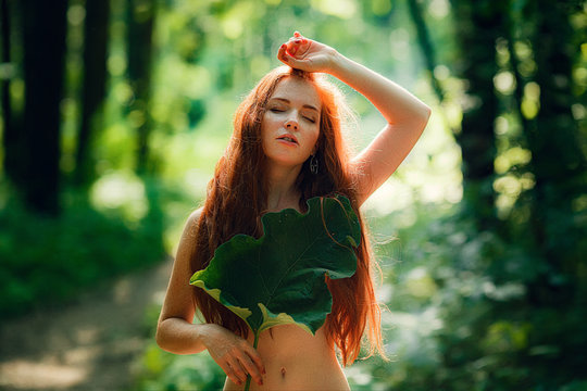 A young ginger woman stand in the green forest.