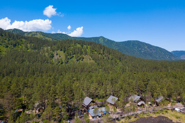 Fototapeta na wymiar Aerial view of cottage for rent on mountain hill resort panorama view with agricultural area in countryside of Altai mountains near river Katun, Russia.