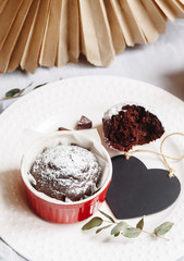 Chocolate muffin in red cup. Mockup valentine black heart copyspace. Small glazed ceramic ramekin with brown cake on a white background.
